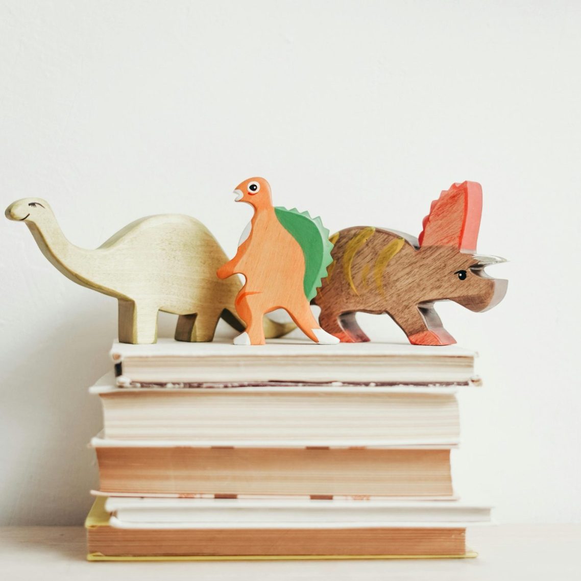 Bunte Dinosaurierfiguren stehen auf einem Stapel Bücher.