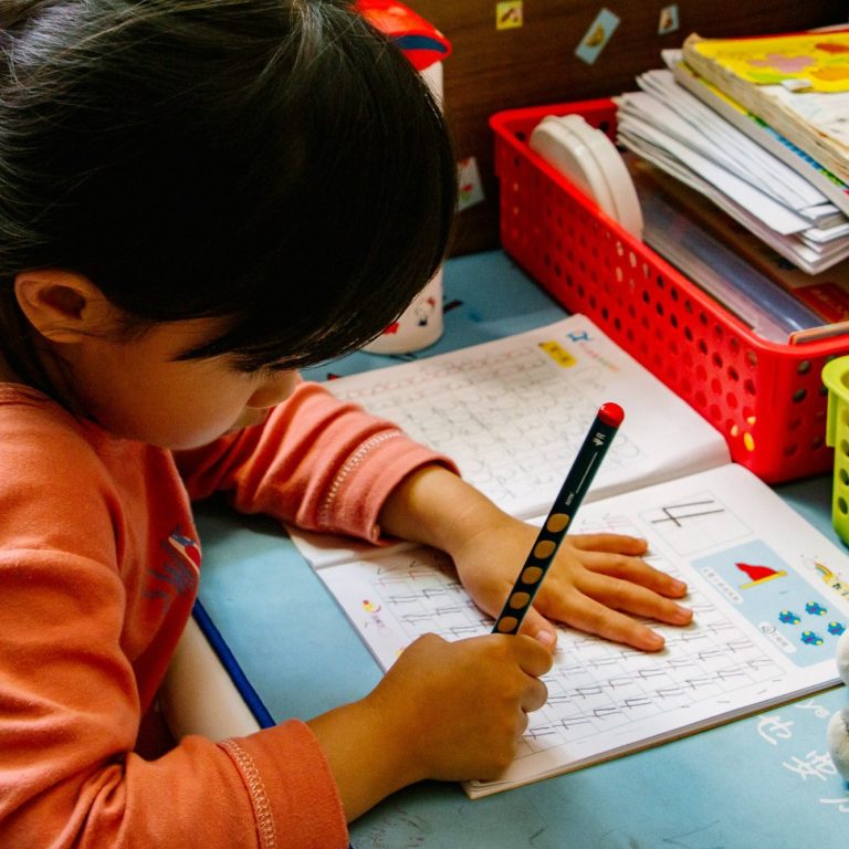 Kind schreibt Ein Kind schreibt in ein Heft, umgeben von Schulmaterial und bunten Behältern.